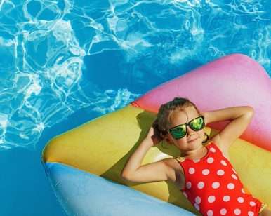 Petite fille avec lunettes de soleil et maillot de bain rouge à pois faisant la sieste sur un matelas gonflable qui flotte dans une piscine.